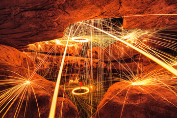 Man wielding spark fire swirl in stone hole cave and pond reflection in the night at Sam Phan Bok