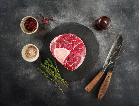 Raw fresh cross cut veal shank and seasonings for making Osso Buco on a slate board with knife.