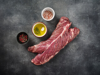 Raw hanging tender or onglet steak of beef on grey background with salt, pepper and olive oil.