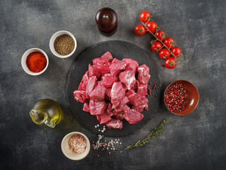 Fresh raw chopped beef on an stone board, spices, herbs and vegetables on dark grey background. Raw...