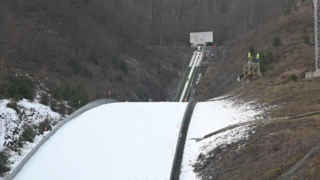 Winter ski jump ramp in Kranj, Slovenia. Jumper runs down to generate sufficient speed before reaching the jump. Person glide down on tracks along the in-run. Handheld, slow motion