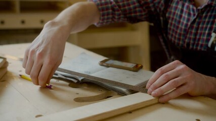 curly joiner master using smartphone checks measurements , handsome Caucasian young man carpenter in apron and caged shirt holding mobile device sitting at work-desk - Powered by Adobe