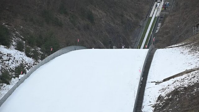 Winter ski jump ramp in Kranj, Slovenia. Jumper runs down to generate sufficient speed before reaching the jump. Person glide in the air over landing slope. Static shot, slow motion