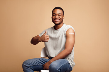 Vaccinated African Guy Gesturing Thumbs-Up After Covid-19 Vaccine Injection, Studio