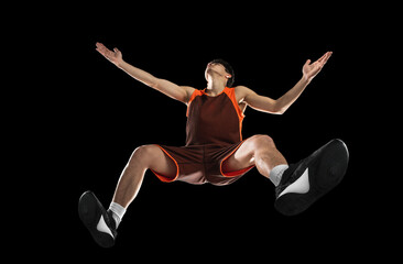 Young professional basketball player in action, motion isolated on black background, look from the...