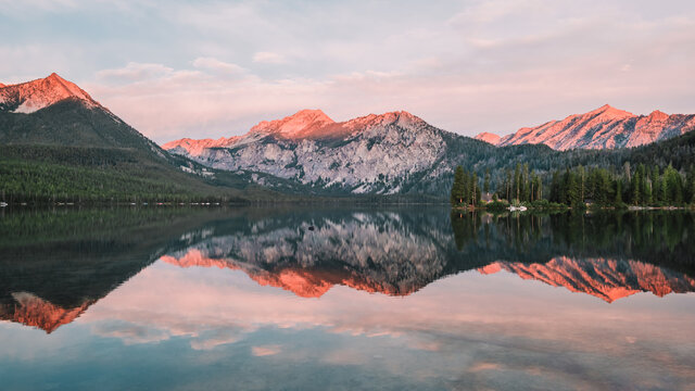 Panoramic landscape of a gorgeous sunrise glow on the peaks of the Sawtooth Mountain Range in the Rocky Mountains and the perfect glass reflections over Pettit Lake in Idaho, USA. © Bella B Photography