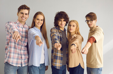 Obraz premium We need you. Join us. Studio group portrait of five happy young people standing together pointing fingers at camera choosing you. Successful college students inviting to become member of their team
