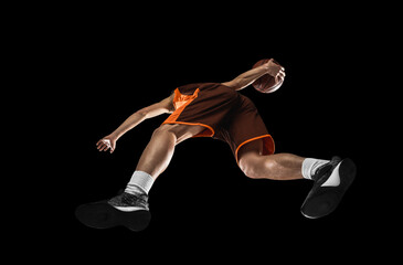 Young professional basketball player in action, motion isolated on black background, look from the...
