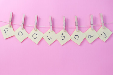 yellow papers on a clothesline.
Yellow papers with the inscription  Fools' Day hang on a clothesline with wooden clothespins on a pink background, close-up side view.