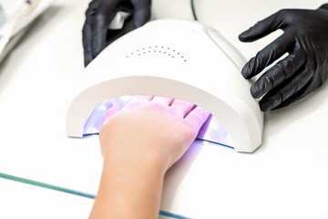 White female hand with manicured nails inside of UV lamp in a nail salon