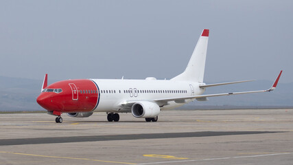 Side view of airplane. Commercial passenger jet airliner taxiing on airport apron, white and red color paint decoration. Modern technology in fast transportation, business travel, charter flights.