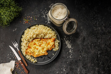 Grilled hawaiian chicken with cheese, ananas and boiled rice served on a black plate