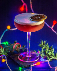 cocktail rosso su sfondo blu, tema natalizio, decorazione con lucine colorate e rametti di pungitopo 