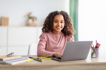 E-Learning. African american girl studying on laptop computer learning at home and smiling to camera