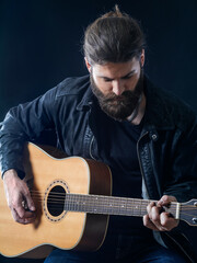Obraz premium Bearded man sitting playing an acoustic guitar
