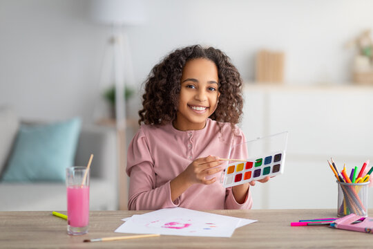 Happy teen girl drawing at home, holding palette and brush, smiling to camera