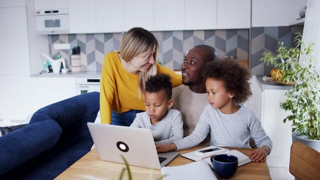 Multi ethnic family and two small children using laptop at home, talking.