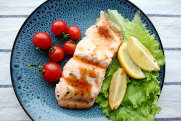 Plate with cooked salmon fillet and tomatoes.
