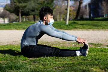 Naklejka na ściany i meble Young man with mask stretching sitting in a park