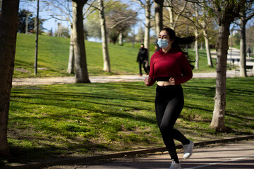 Young woman with face mask because covid, running in the park. Active person outdoors.