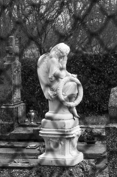 Old cemetery with mourning angel on the tomb holding wreath with word souvenir (memory in French) seen through fence. France. Grief, loss, sadness concepts. Religious background. Black white photo.
