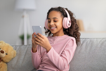 Leisure concept. Happy girl listening to music in wireless headphones, chatting on her smartphone