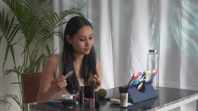 Beautiful Asian woman watching makeup tutorial video ,learning how to do make-up in online on PC tablet. Indian girl learning makeup in online class at home.Video makeup tutorial and vlogging concept.
