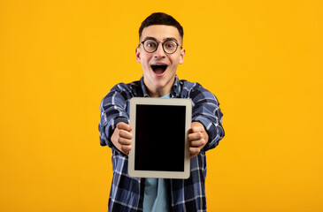 Overjoyed millennial man showing tablet computer with mockup for website or app design on orange background