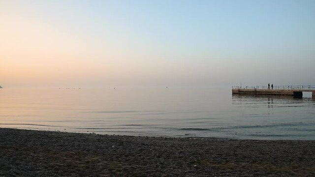 San Simon bay, Slovenia: concrete pier with calm waves hitting pebble beach at sunset. Beautiful colors at golden hour. Static shot, real time, wide angle