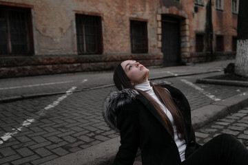 Fototapeta na wymiar a girl sits on a city street, her head thrown back, looks up