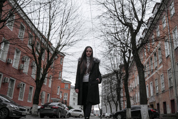 Fototapeta na wymiar a girl in a black coat walks along an old European street