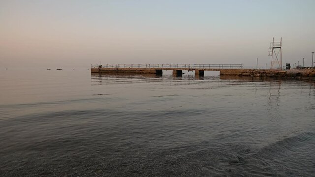 San Simon bay, Slovenia: concrete pier with calm waves hitting pebble beach at sunset. Beautiful colors at golden hour. Static shot, real time, wide angle