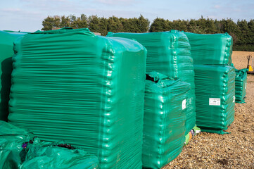 Pallets stacked in a row  with green shrink wrapping around the sacks of garden manure.