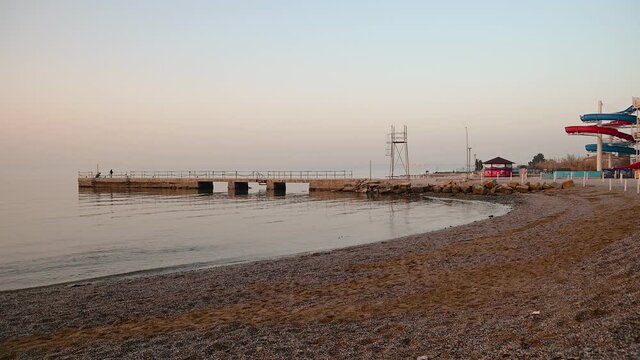 San Simon bay, Slovenia: concrete pier in winter. Calm waves hitting pebble beach at sunset. Beautiful colors at golden hour. Static shot, real time, wide angle