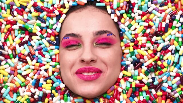 Artistic image of a beautiful woman sunk inside colored pills and capsules. 
