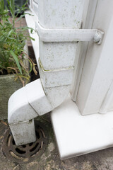 Dirty clogged white plastic pvc gutters and drain pipes with mossy green mould on plastic fascias. ...