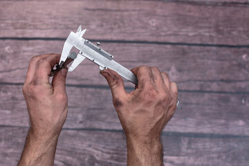 The worker measures the diameter of the drill with a caliper. His hands were dirty from his work....