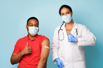 Fototapeta na wymiar Vaccinated African Man And Nurse Gesturing Thumbs-Up Over Blue Background