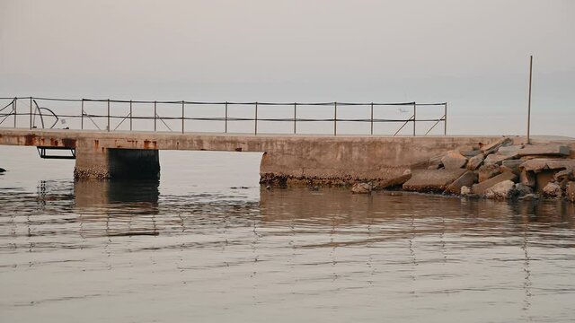 San Simon bay, Slovenia: empty concrete pier in winter. Calm waves at sunset. Beautiful colors at golden hour. Static shot, real time