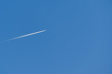 Minimalist background of an airplane leaving a trail while flying through a cloudless sky