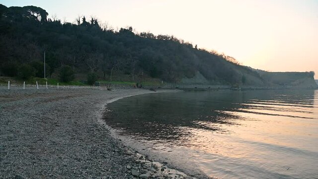 Calm waves gently hitting coastline at sunset. Beautiful evening on Adriatic Sea. Coast of Slovenia. Pebbles in San Simon bay. Beautiful light in twilight. Static shot, real time, wide angle