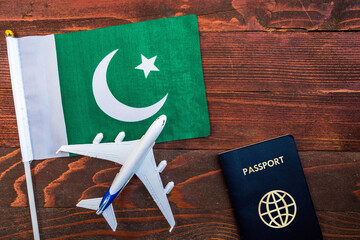 Flag of Pakistan with passport and toy airplane on wooden background. Flight travel concept.