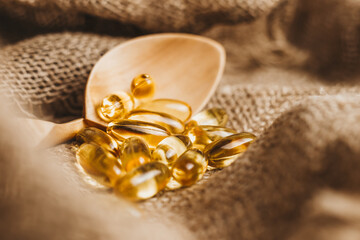 Fish oil capsules on a wooden spoon. Fish oil pills, tablets on the burlap. Vitamin complex omega 3,6,9. Fish oil capsules with omega-3, vitamin D. Copy space