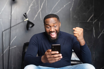 Goal achievement. Overjoyed African-American businessman looks at the smartphone screen and...