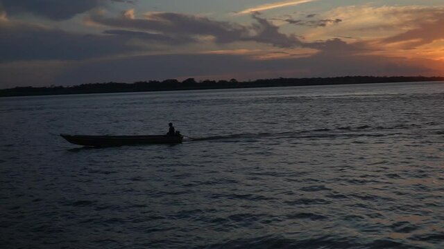 Beautiful sunset on the Rio Amazonas River. Silhouette view of man sailing on boat with sun at dusk and night background in Amazon Rainforest. Concept of ecology, environment, conservation.