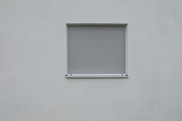 grey closed window shutter on a  bright stone wall,
space for text, no person