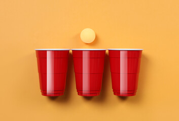 Plastic cups and ball for beer pong on orange background, flat lay - obrazy, fototapety, plakaty