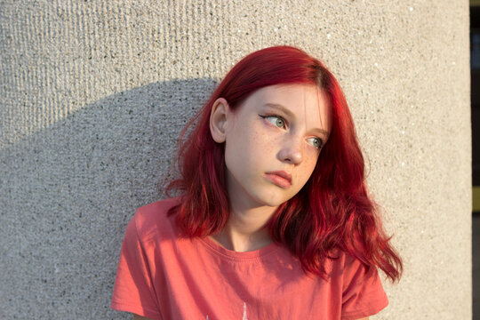 A serious teenage girl with dyed red crimson hair and freckles. City portrait at sunset.