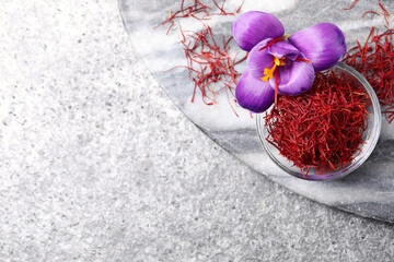 Dried saffron in bowl and crocus flowers on grey table, flat lay. Space for text