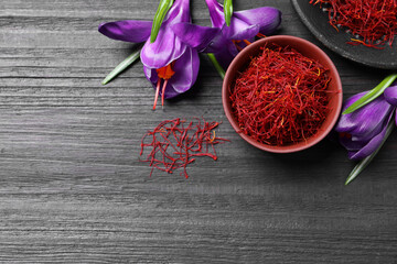 Obraz na płótnie Canvas Dried saffron in bowl and crocus flowers on black wooden table, flat lay. Space for text